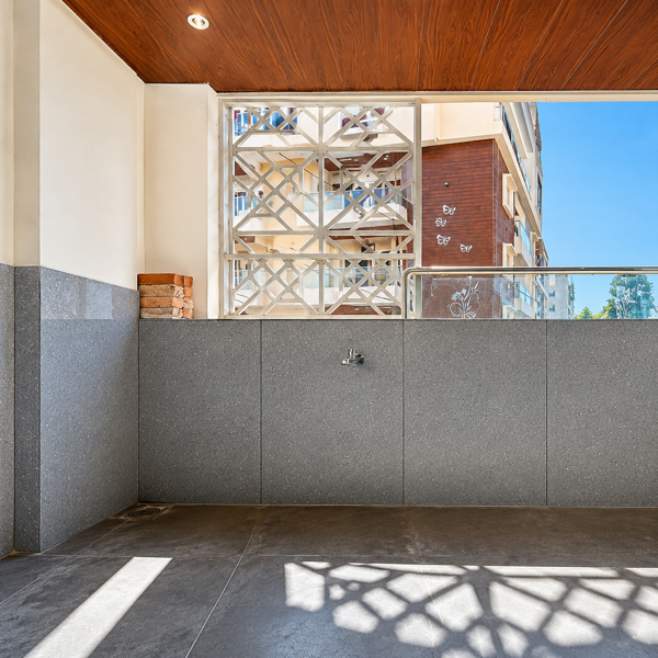 Modern architecture, residential, balcony, entrance, porch, car parking, covered parking, granite wall, granite flooring, grey granite, stone cladding, wooden ceiling, wooden paneling, recessed lighting, natural light, geometric grille, decorative grille, metal railing, glass railing, stainless steel railing, exterior building, apartment, residential building, urban architecture, contemporary design, textured wall, clean lines, neutral colors, brown flooring, polished surface, sunlight, shadows, patterned shadows, blue sky, daylight, ventilation, open space, architectural details, facade, exterior design, parking area, tiled floor, wall tap, water outlet, brick stack, construction materials, elegant interior exterior, minimalist design, modern home, luxury residence, geometric patterns, bright atmosphere.